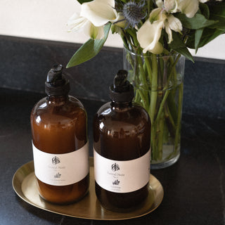Jack's Daughters Santal Noir No. 1 Soap and Lotion Jars on Suna Brass Tray on Counter Next to Vase of Flowers